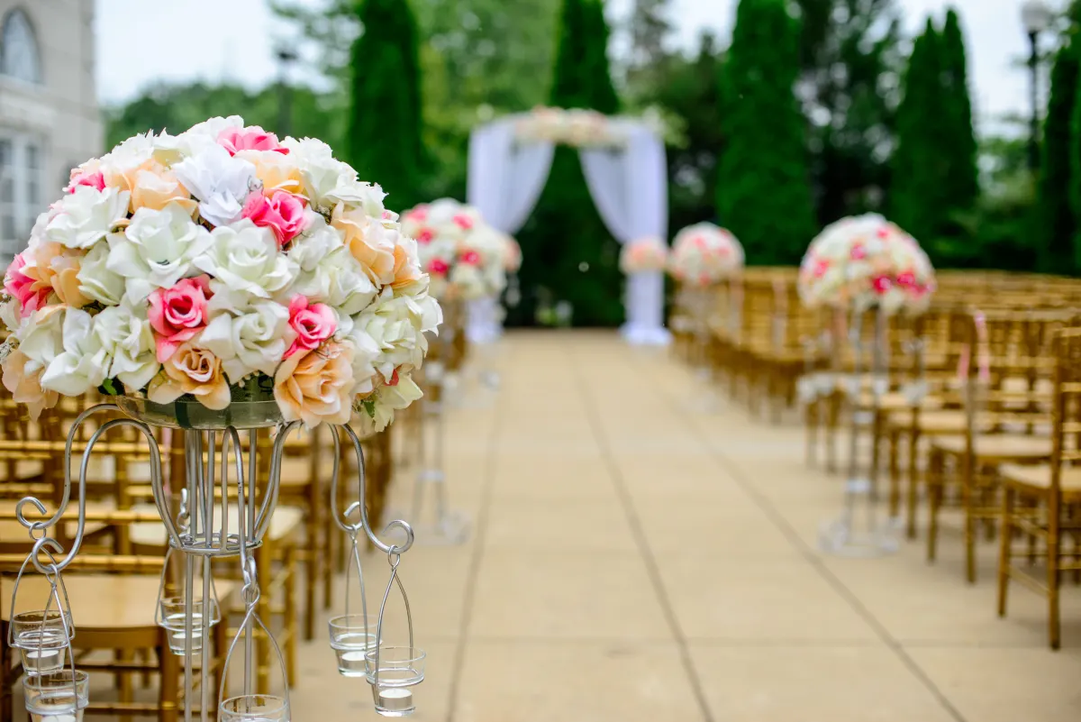 Rows of gold chairs and flower arrangements along an outdoor wedding aisle